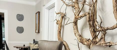 Ein Wohnzimmer mit zwei grauen Sesseln, einem Holztisch und einer großen Wanddekoration aus einem Ast.