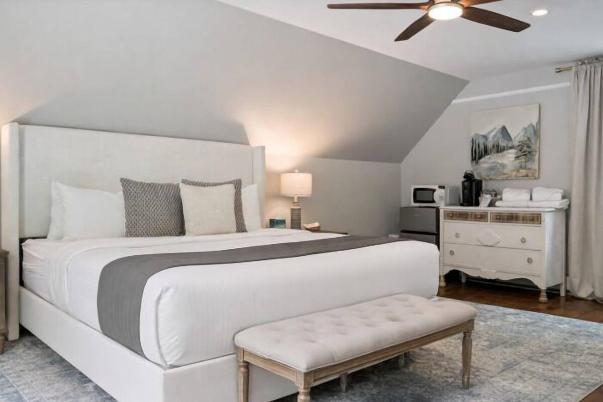 A bedroom with a bed, bedside table, lamp, dresser, and a ceiling fan.