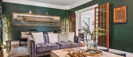 Ein Wohnzimmer mit dunkelgrüner Wand, einem Holztisch, einer Couch und einer großen Holztür mit Glasscheiben.
