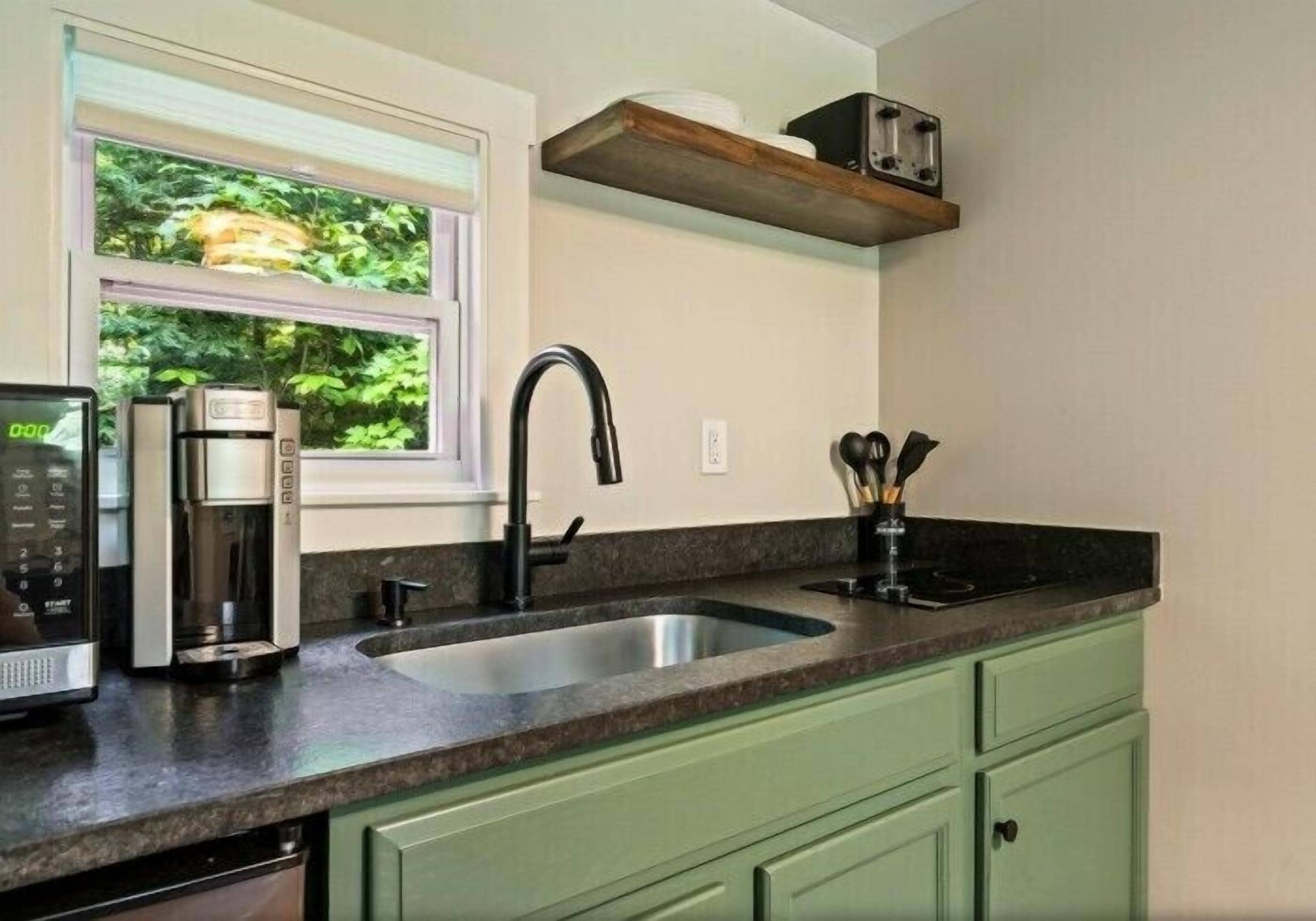A kitchen with a built-in coffee maker, a sink, and a window with a view of greenery.