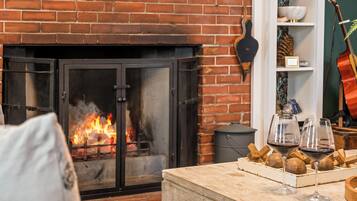 Una sala de estar acogedora con chimenea, una mesa de madera con copas de vino y pan, y una guitarra al fondo.