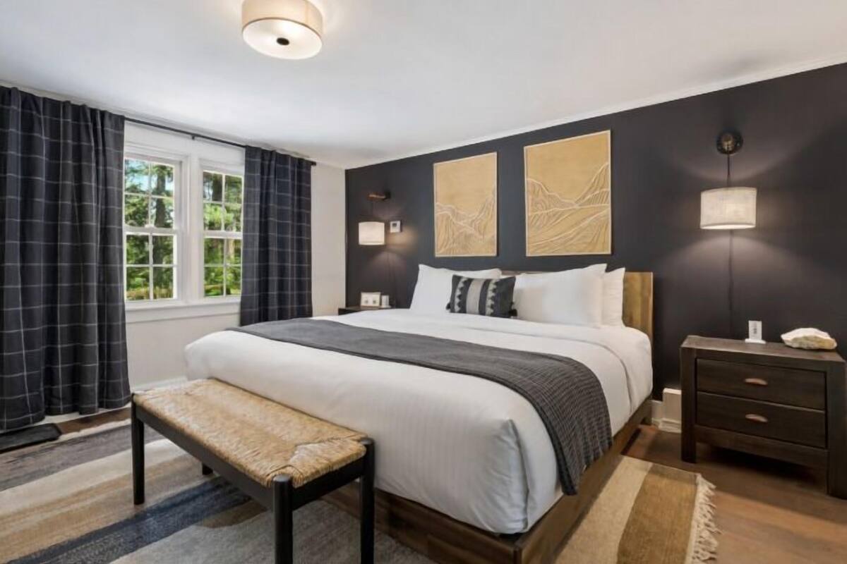 A bedroom with a large bed, bedside tables, a bench, and artwork on the walls.