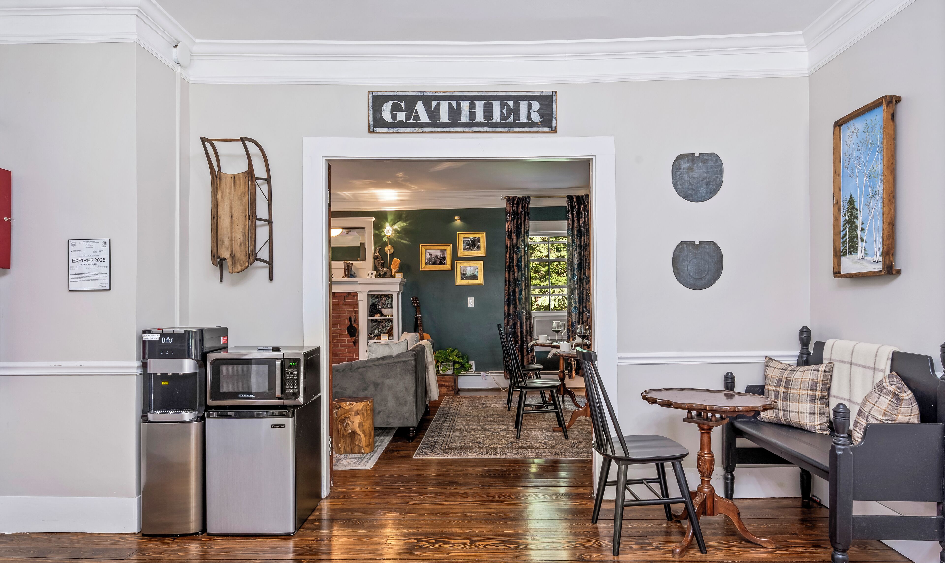Un salon chaleureux avec un panneau indiquant « GATHER », un coin repas avec une table ronde et des chaises, et une cuisine équipée d’appareils électroménagers.
