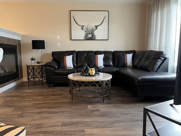 A living room with a sectional sofa, a round coffee table, and a fireplace. - 2 bedroom upper level of home in Grande Prairie  (Grande Prairie)