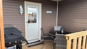 En overdækket veranda med grill, spisebord med stole, en dør og et skilt med teksten "Relax & Unwind Patio Time".