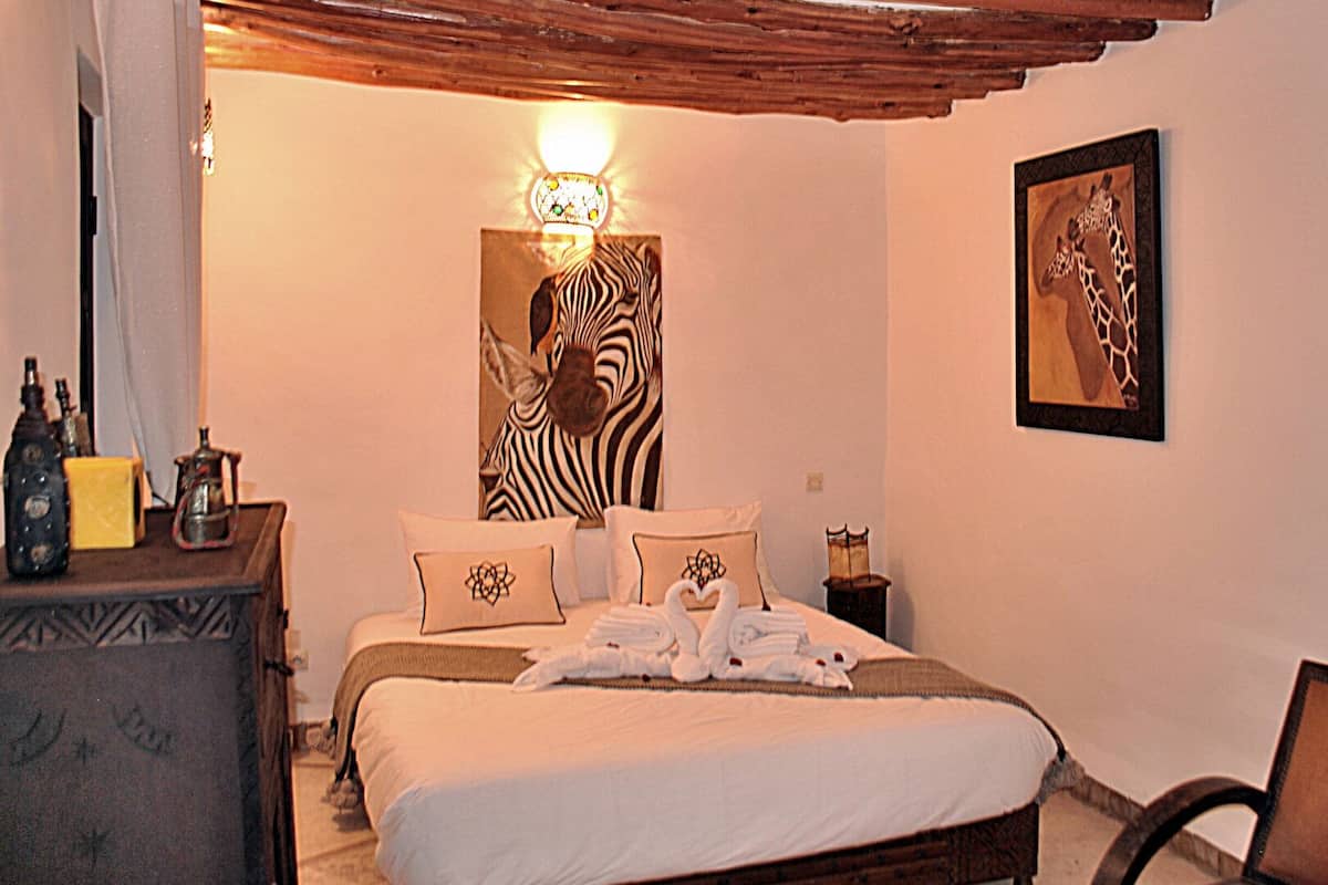 A bedroom with a zebra painting, a giraffe painting, and a bed with towels.