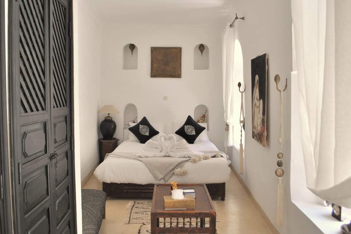 A bedroom with a bed, a bedside table, a window with curtains, and a door.