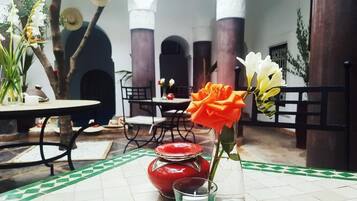 Un coin repas avec une table dressée pour deux personnes, un vase rempli de fleurs et un mur décoratif agrémenté de détails architecturaux.