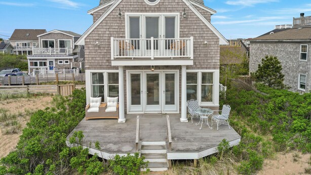 A two-story house with a balcony, large windows, and a deck with outdoor furniture.