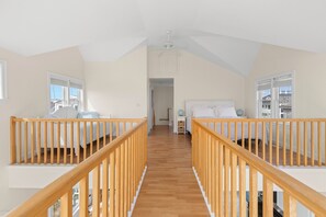A spacious loft bedroom with a wooden staircase, a large bed, and a view of the city.