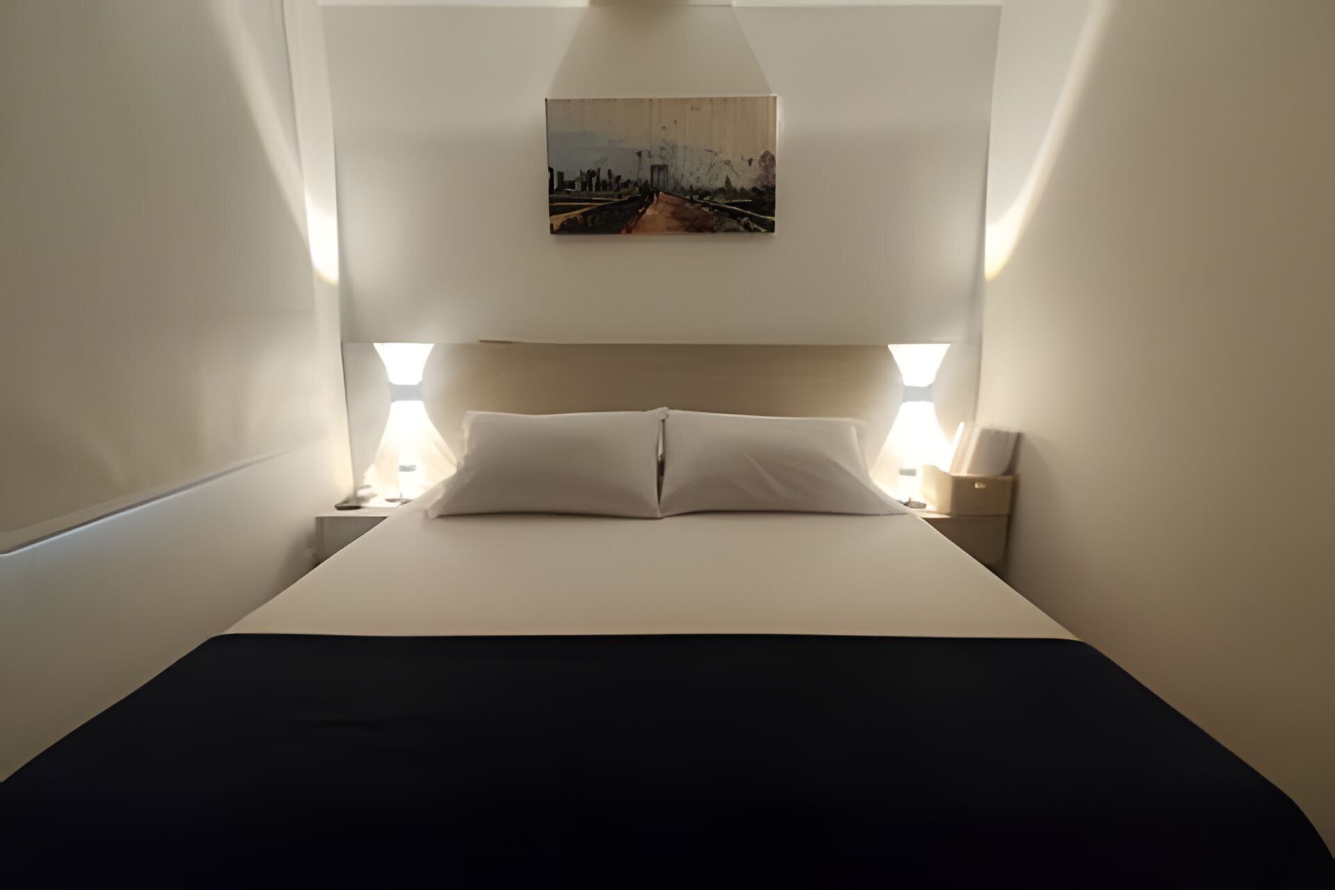 Una habitación de hotel con una cama, dos lámparas de noche y un cuadro en la pared.