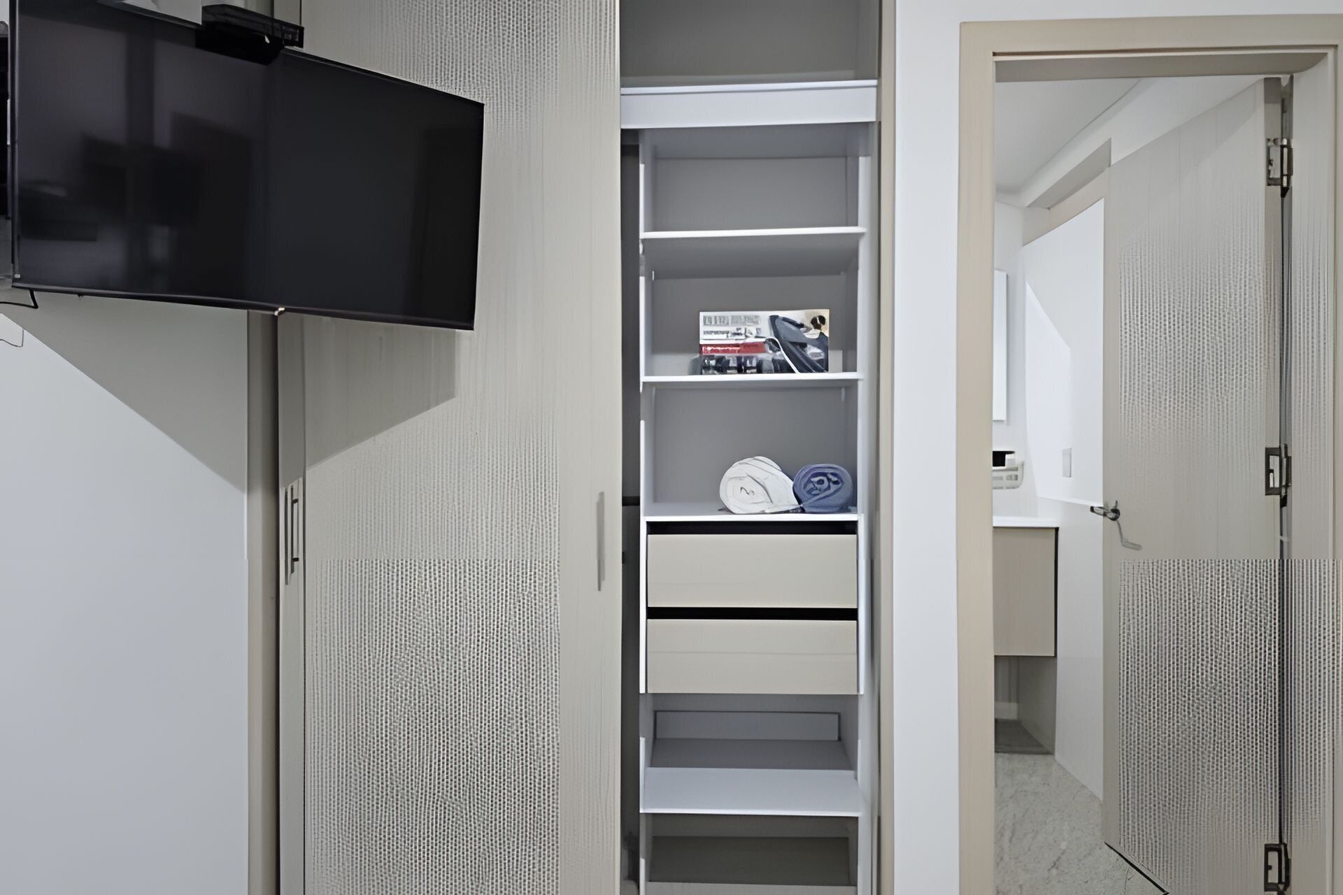 Un vestidor amplio con un televisor en la pared, repisas con ropa doblada y una puerta que da a otra habitación.