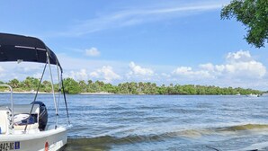 A boat docked at a sandy beach with a clear view of the water and a forested shoreline in the background.