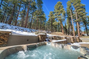 Une zone de sources chaudes avec des murs en pierre et une piscine, entourée de grands pins et recouverte de neige.
