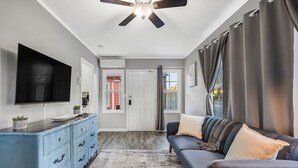 A modern living room with a flat-screen TV, a blue dresser, a gray sofa, and a ceiling fan.