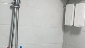 Una ducha con un cabezal de ducha cromado y un perchero de pared con dos toallas blancas.