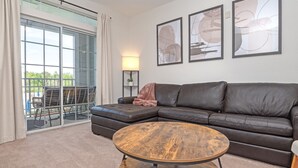 A modern living room with a leather sofa, a round coffee table, and a glass door leading to an outdoor area. - Disney Fab4, Stitch, Lady!Come enjoy a Magical vacation so close to WDW and more (Kissimmee)