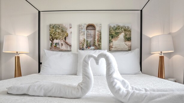 A neatly made bed with white linens and pillows, two bedside lamps, and three framed artworks on the headboard. - Disney Fab4, Stitch, Lady!Come enjoy a Magical vacation so close to WDW and more (Kissimmee)