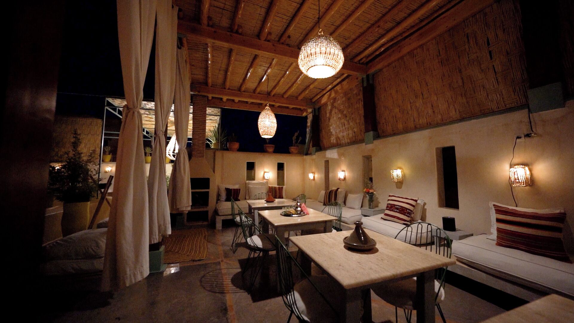 Un comedor acogedor y rústico con vigas de madera, una araña y una variedad de asientos, incluyendo mesas y un sofá.
