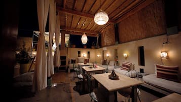Un comedor acogedor y rústico con vigas de madera, una araña y una variedad de asientos, incluyendo mesas y un sofá.