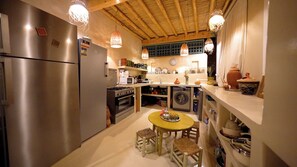 Eine kompakte Küche mit Kühlschrank, Herd, Backofen, Mikrowelle und Waschmaschine. Ein kleiner Esstisch mit Hockern steht bereit.