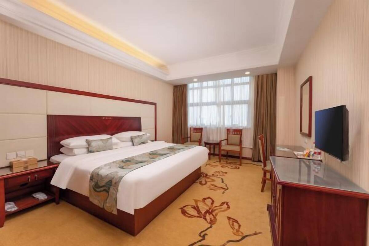 A hotel room with a large bed, a desk, a chair, a TV, and a window.