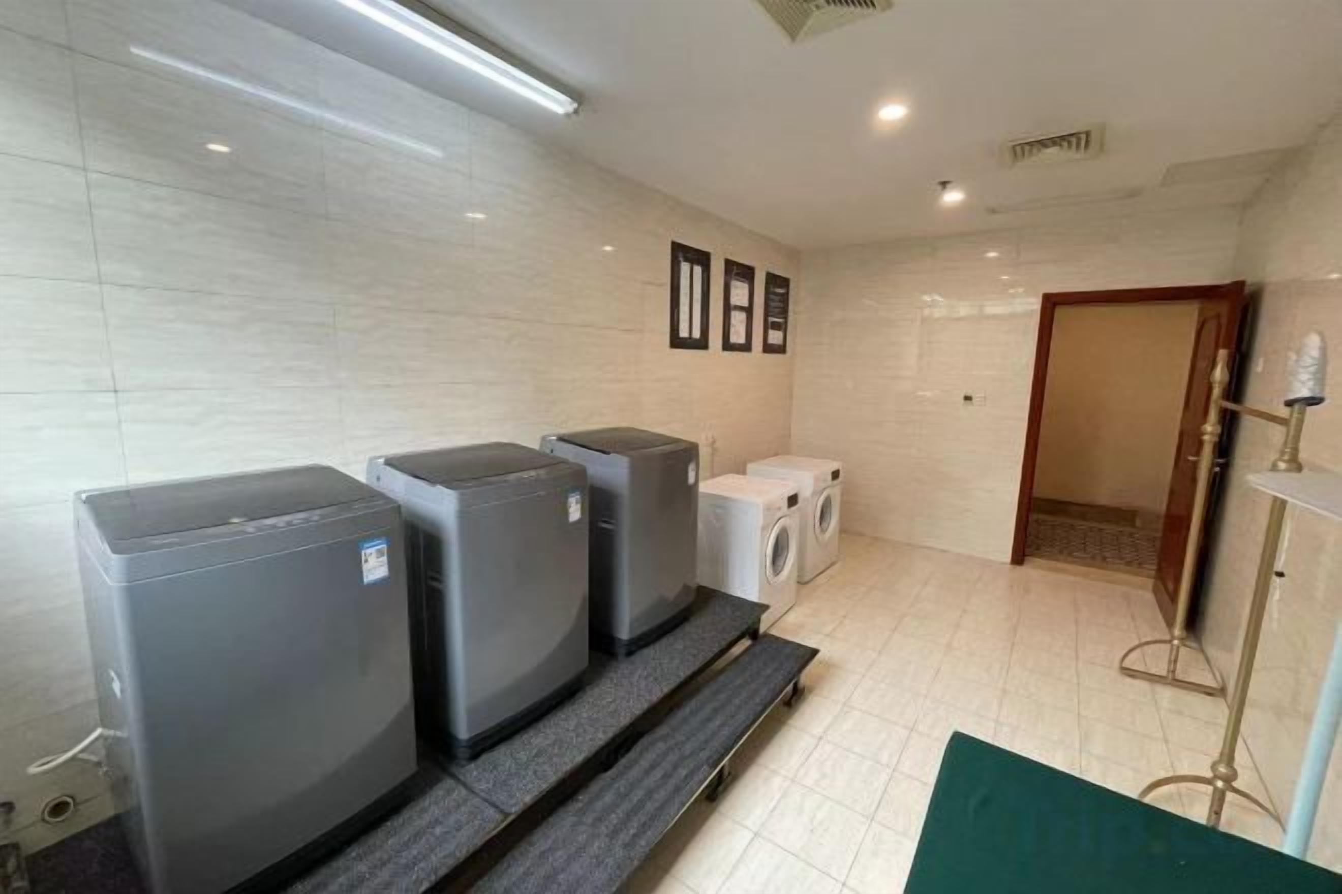 A hotel bathroom with three large, dark-colored washing machines, a white toilet, and a mirror on the wall.