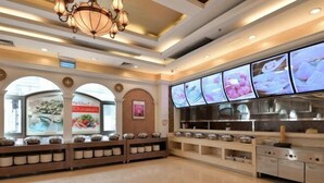 A modern restaurant interior with a central serving counter, overhead lighting, and digital menu displays.