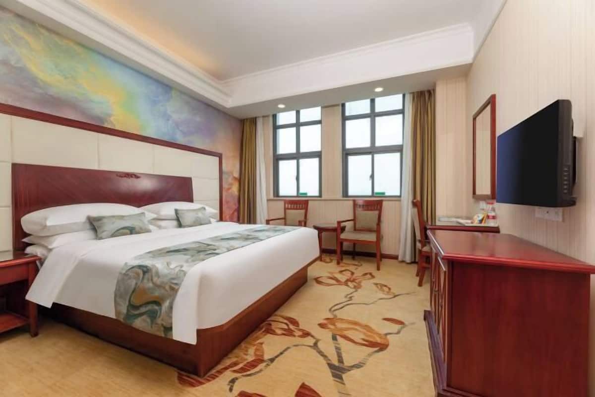 A hotel room with a large bed, a desk, a chair, a television, and a window with curtains.