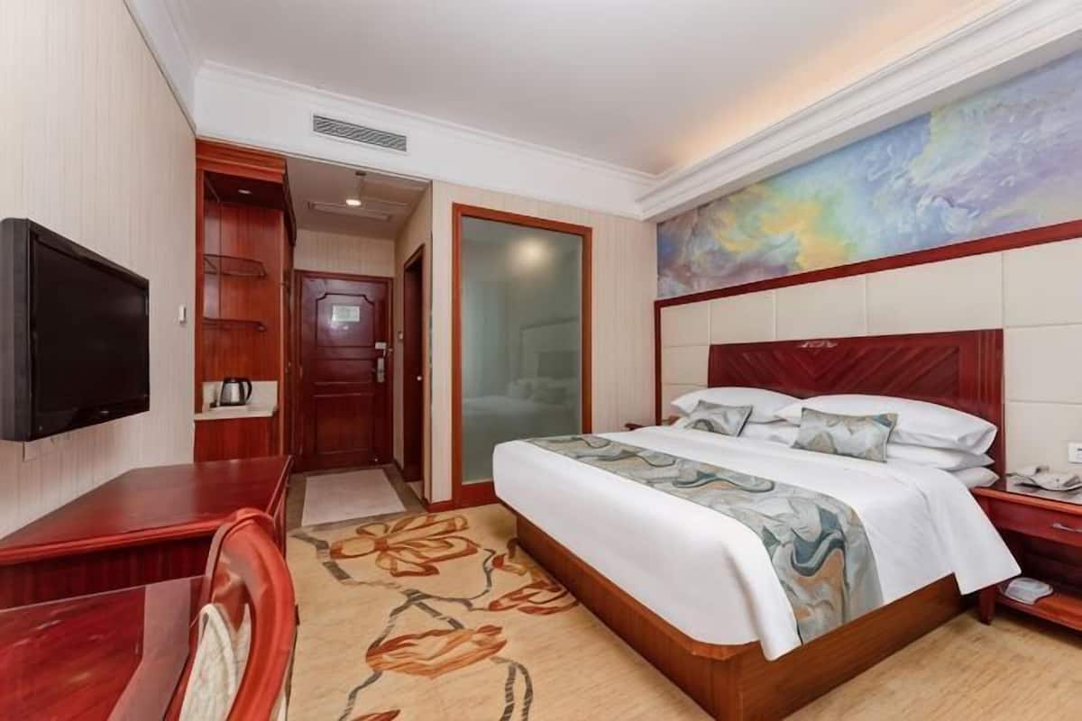 A hotel room with a bed, a television, a desk, and a door leading to a bathroom.