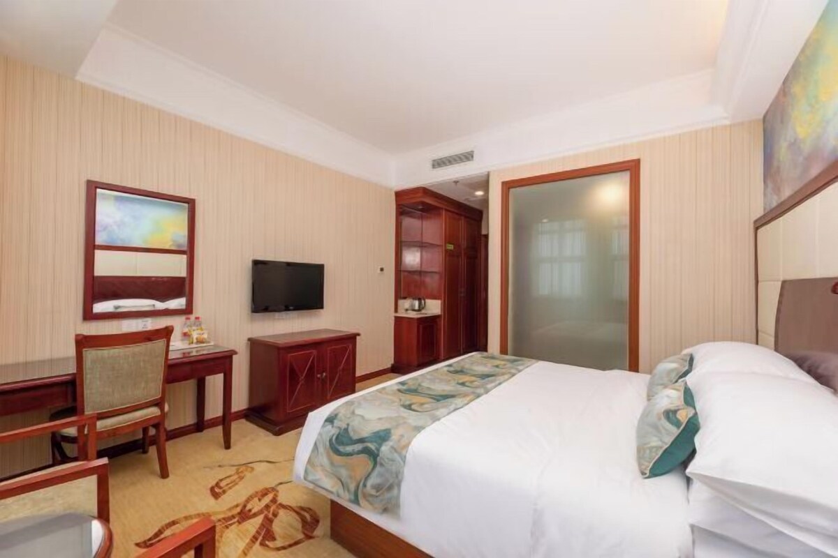 A hotel room with a bed, a desk with a chair, a television, and a wardrobe.