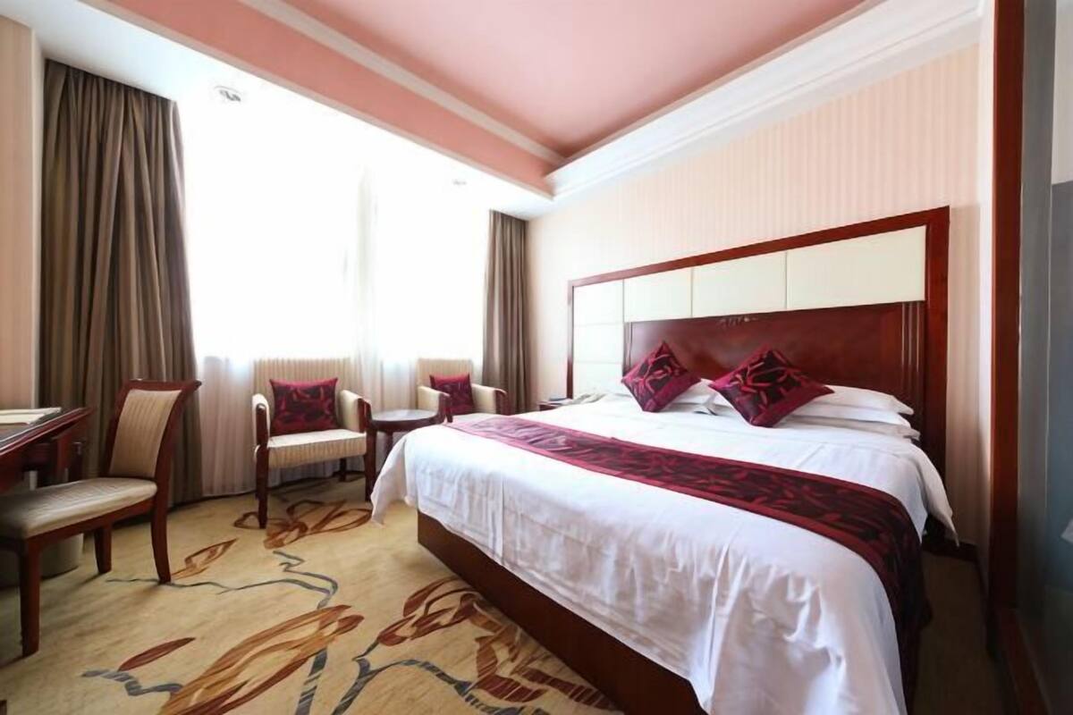 A hotel room with a large bed, two chairs, a desk, and a window with curtains.