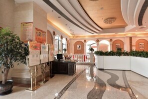 Un vestíbulo de hotel con mostrador de recepción, plantas en macetas y una pared curva.