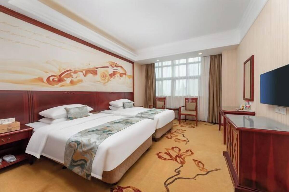 A hotel room with a large bed, a desk, a TV, and a painting on the wall.