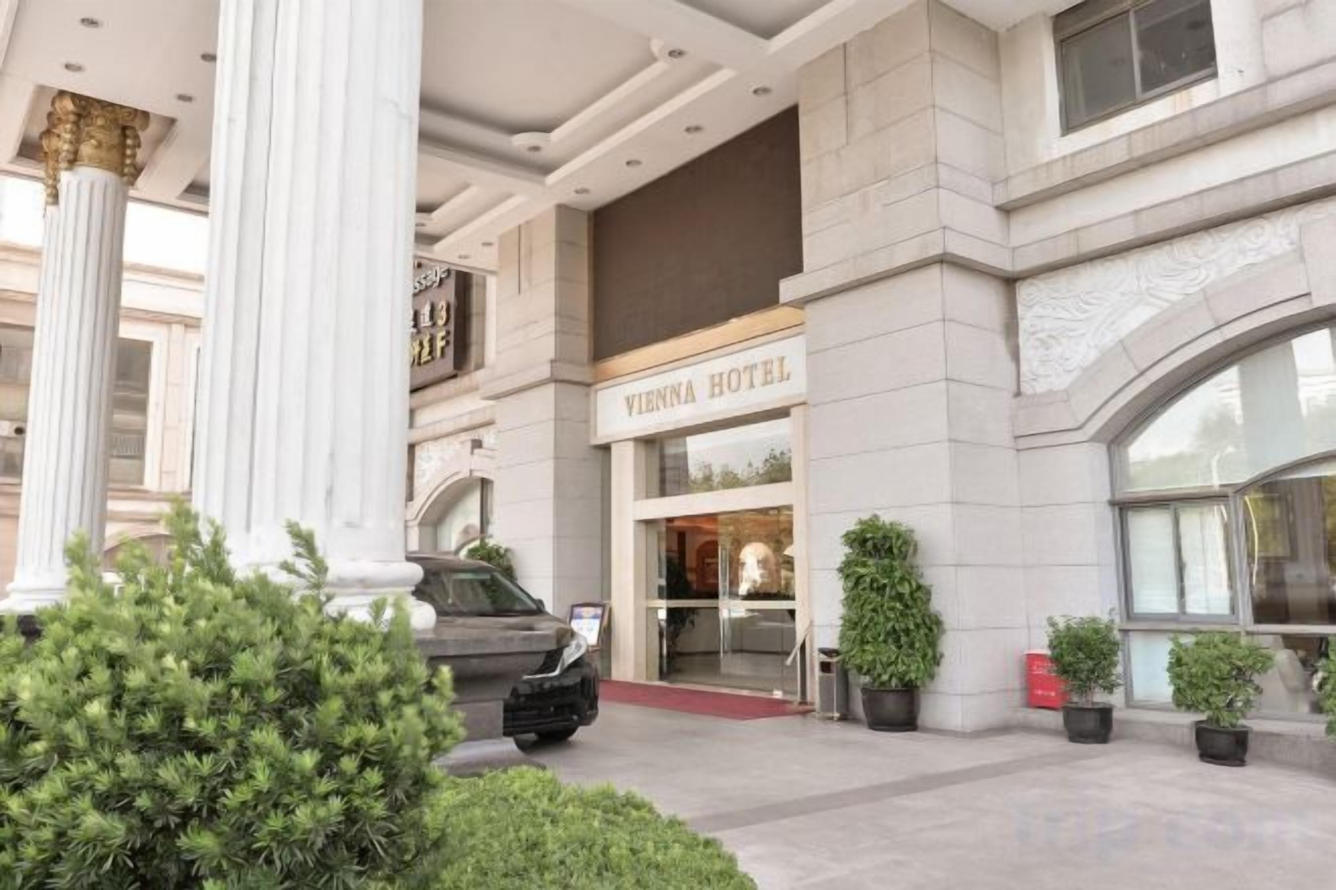 A Vienna Hotel entrance with a grand facade, columns, and potted plants.