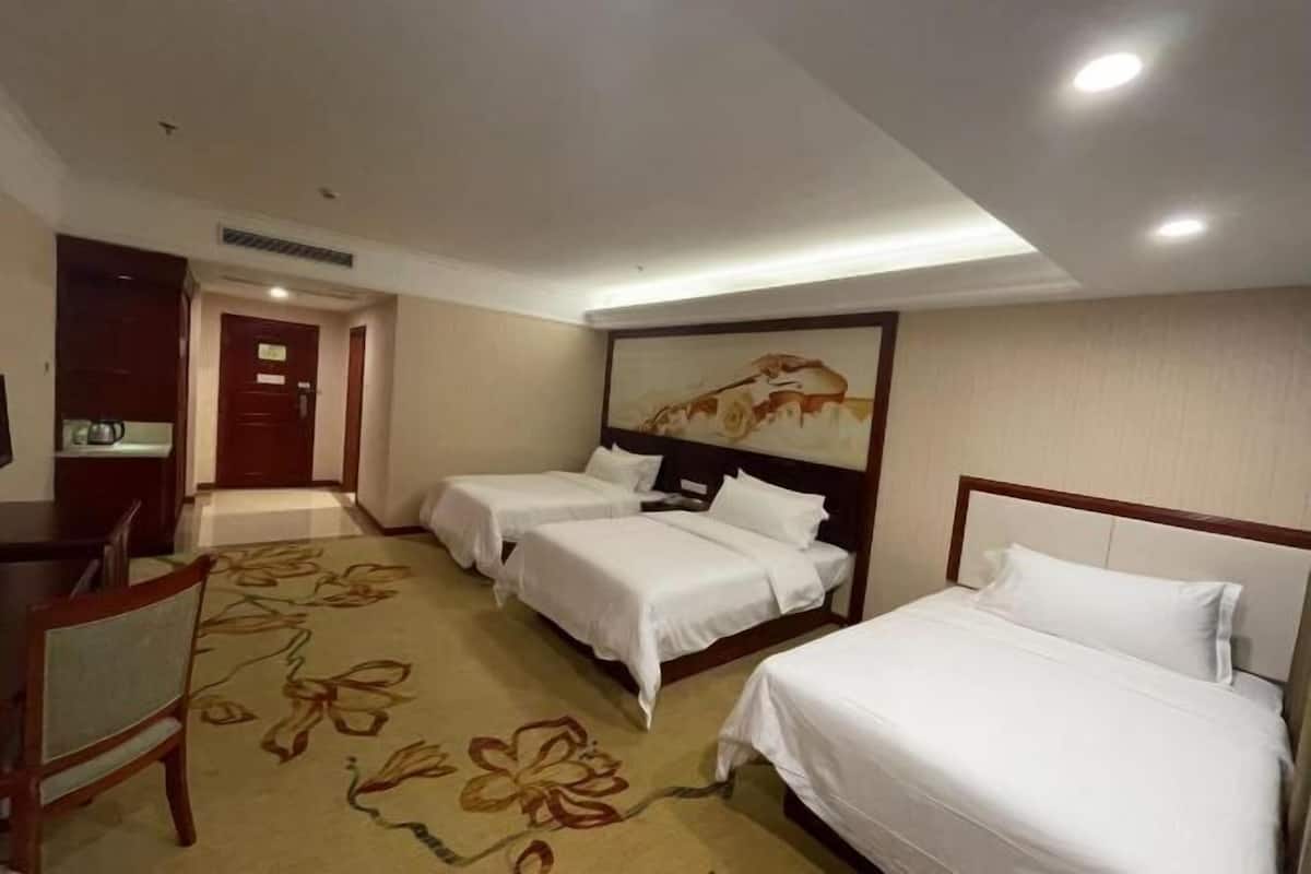 A hotel room with two single beds, a desk, a chair, and a large painting on the wall.