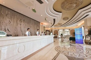 A hotel reception area with a marble wall, a reception desk, and a decorative ceiling.