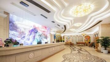 A hotel lobby with a reception desk, a large abstract mural, a chandelier, and a patterned carpet.