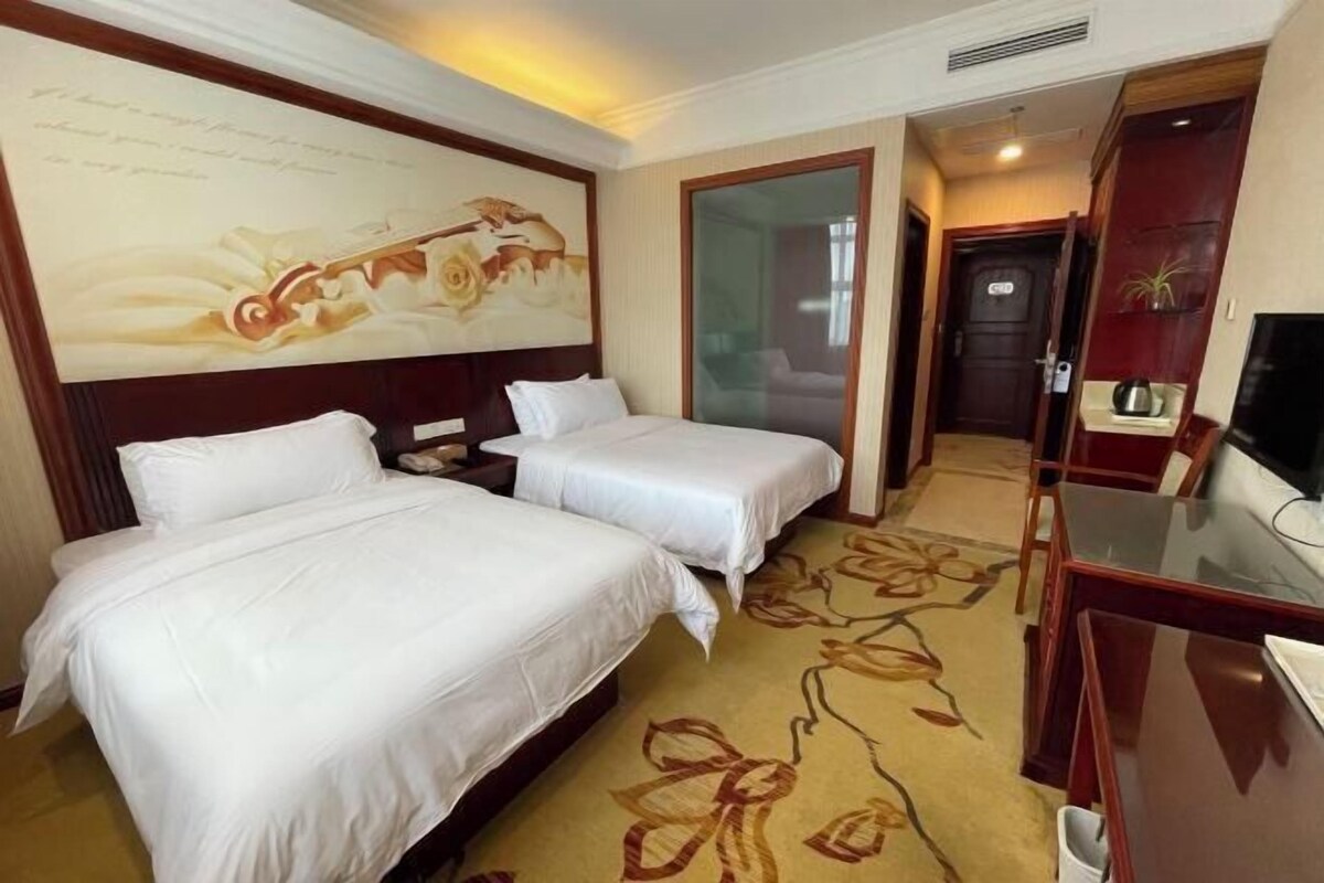 A hotel room with two beds, a large mirror, a television, and a floral carpet.