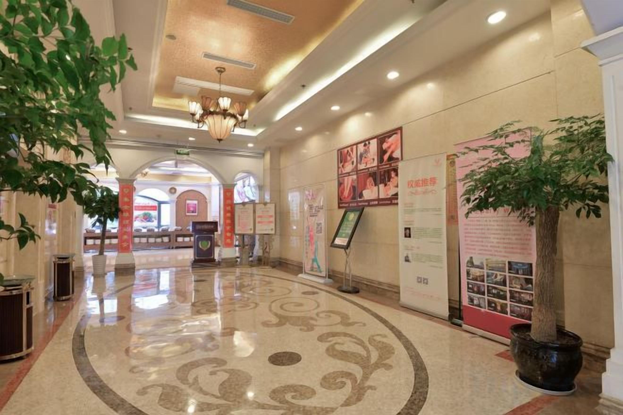A hotel lobby with a polished floor, a chandelier, and a large potted plant.