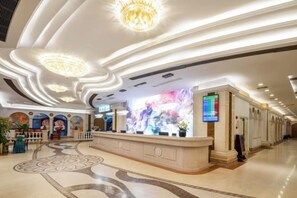Un hall d’hôtel comprenant un comptoir d’accueil, un grand écran numérique et un sol à motifs.