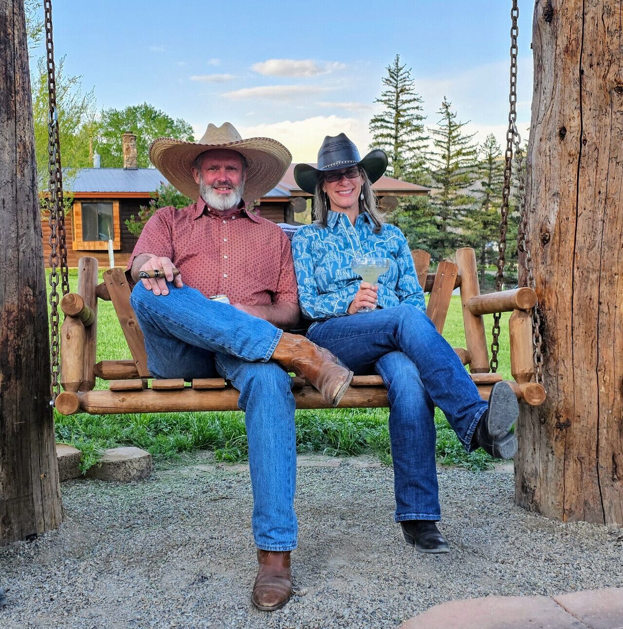 A wooden swing set with two people sitting on it, surrounded by a gravel path and greenery.
