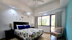 A bedroom with a bed, a chair, a nightstand, a ceiling fan, and a window with curtains. - Casa Azules Jungle Villa 3 piscinas near the beach (Venado)