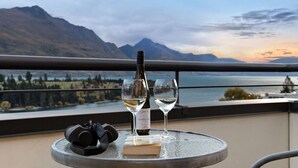 A balcony with a table holding a wine bottle and glasses, overlooking a mountainous landscape and a body of water. - Swallowdale | A home away from home, close to town (Queenstown)