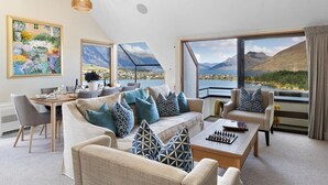 A modern living room with a large window offering a scenic mountain view, a dining area with a table set for two, and a cozy seating arrangement with patterned cushions. - Swallowdale | A home away from home, close to town (Queenstown)