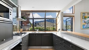 A modern kitchen with a large window, stainless steel appliances, and dark cabinetry. - Swallowdale | A home away from home, close to town (Queenstown)