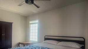 Ein Schlafzimmer mit einem Bett, einem Fenster, einem Deckenventilator und einem dunklen Holzschrank.