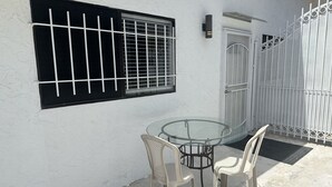 Ein Glastisch mit zwei Stühlen, ein Fenster mit Metallgitter und eine weiße Tür mit Metalltor.