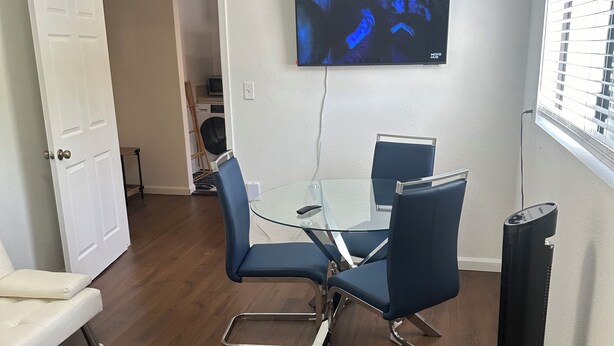 Ein modernes Wohnzimmer mit einem Glastisch, blauen Stühlen, einem weißen Sofa, einem wandmontierten Flachbildfernseher und einem Standheizgerät.