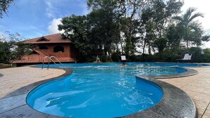 Una piscina de diseño curvo, rodeada de una zona pavimentada y un edificio con tejado de azulejos.